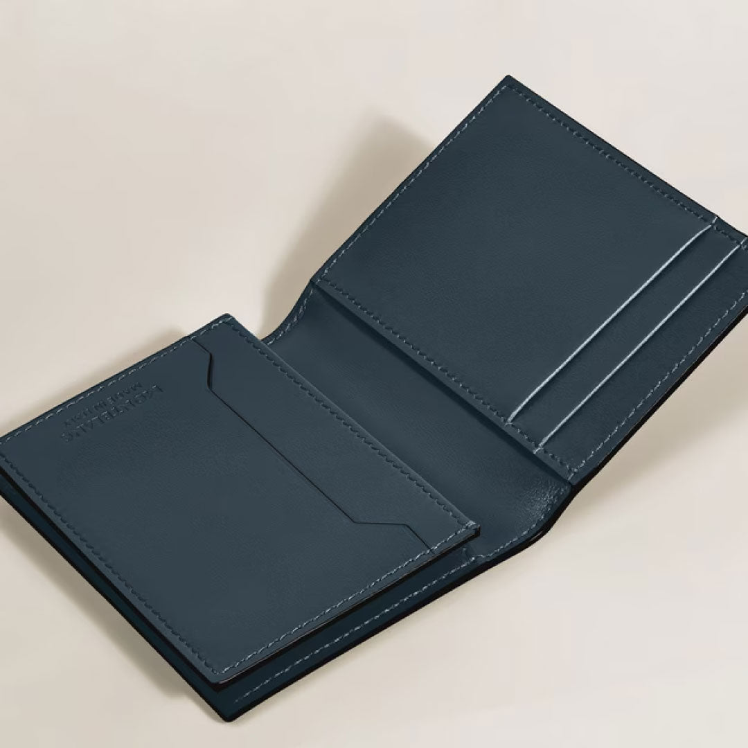 The Montblanc Meisterstuck 4CC Leather Card Holder features blue velvet calfskin leather with two card slots on the left and a bill compartment on the right, elegantly displayed on a light-colored surface.