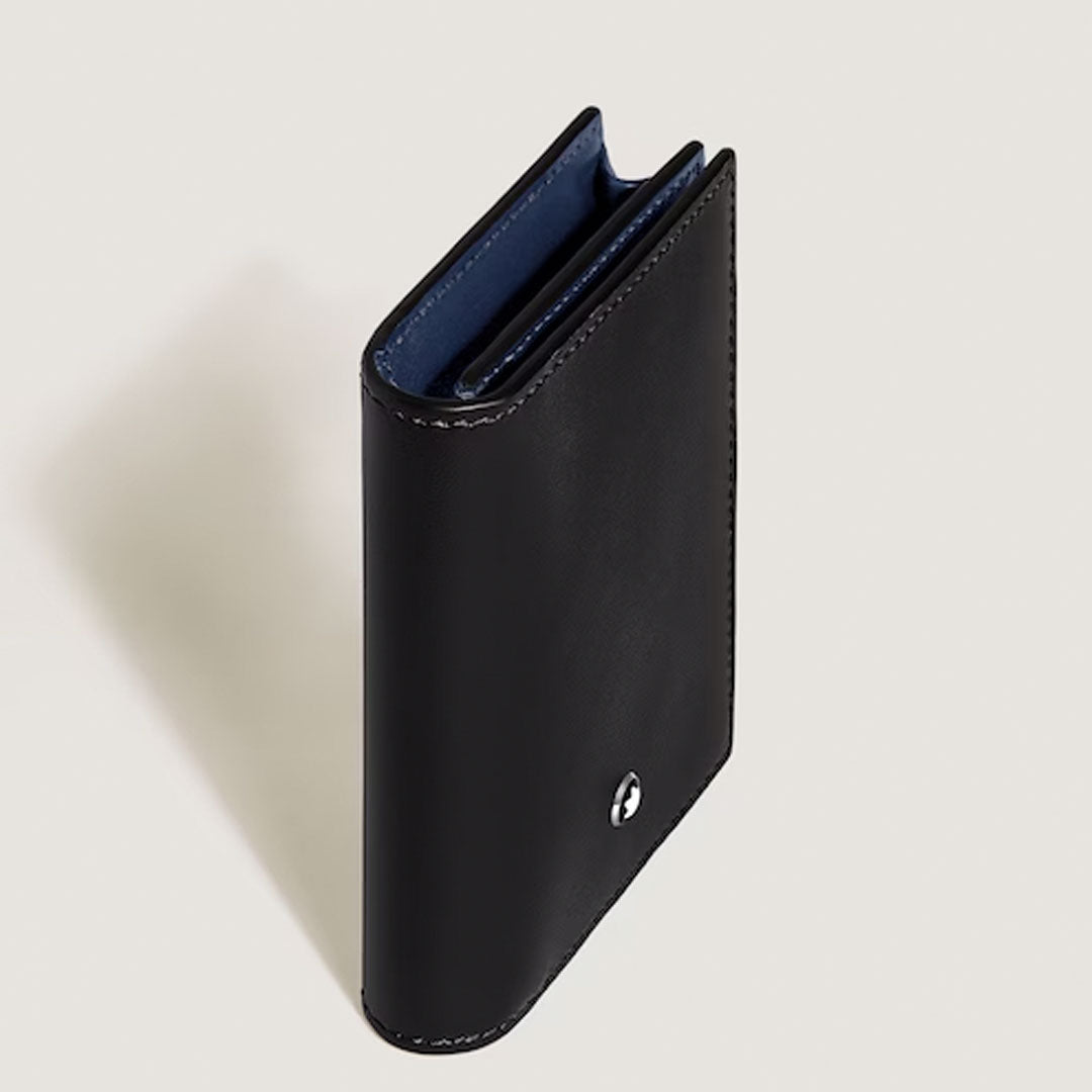 The Montblanc Meisterstuck 4CC Leather Card Holder, in black leather with visible stitching and a round silver Montblanc emblem on the front, stands upright on a light surface, showcasing its branded credit card slots.