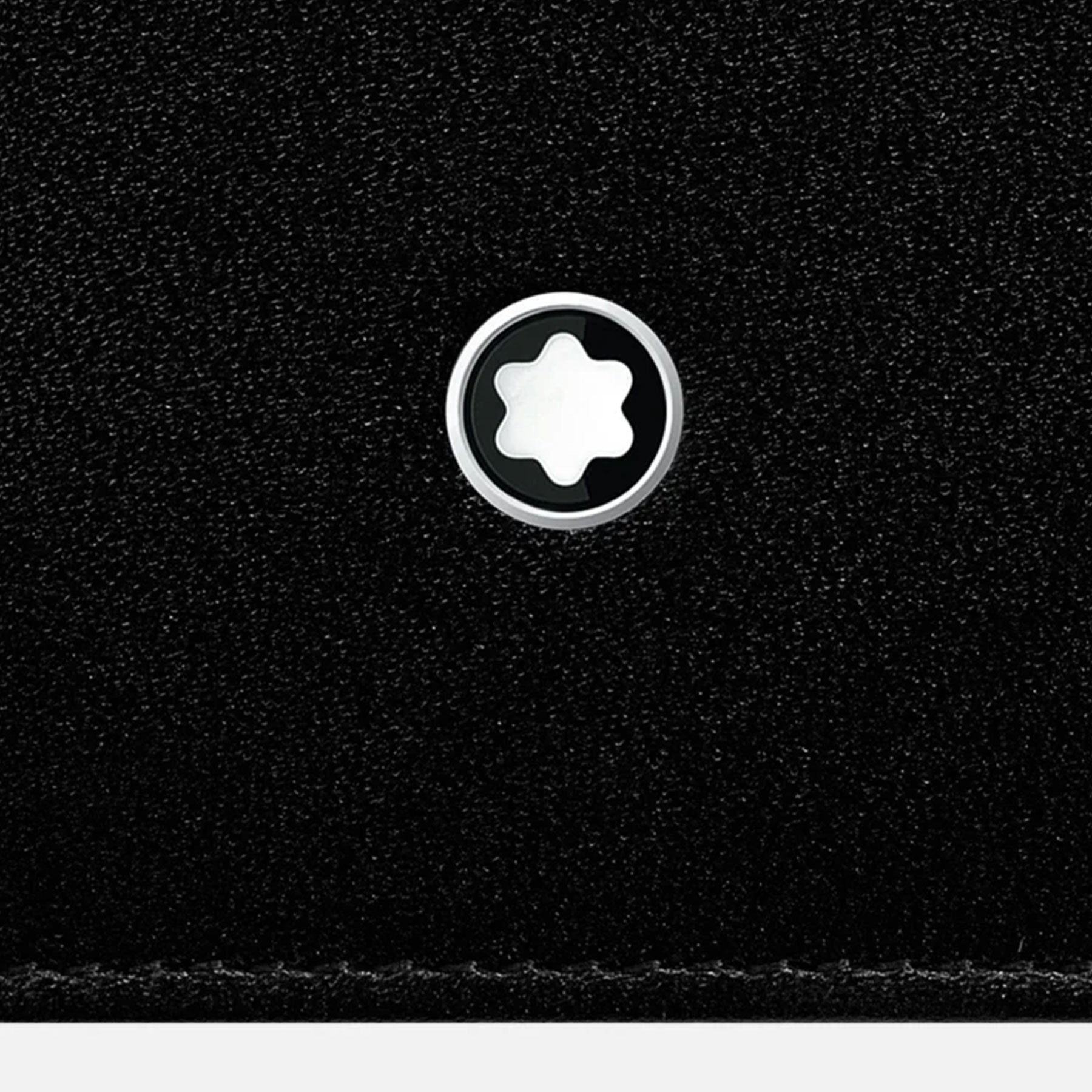 Close-up of the Montblanc Meisterstück Black Leather Wallet's full-grain cowhide leather surface showcasing a metallic circular emblem adorned with a white star design at its center.