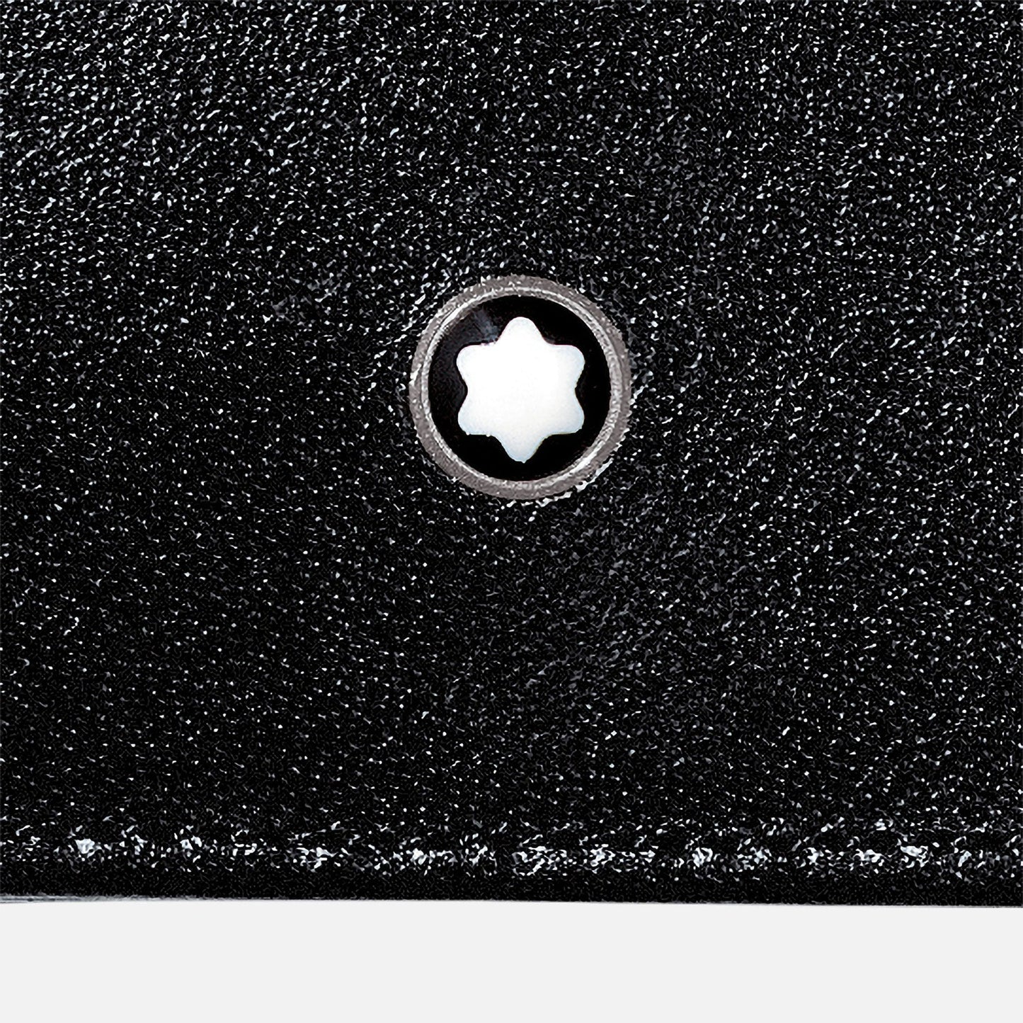 A close-up image of the Montblanc Meisterstuck 8cc Leather Wallet in black leather displays a round white emblem featuring a star-like pattern at the center, framed by a metallic rim. The subtle European full-grain cowhide texture enhances its appearance, accented by visible white stitching along the bottom edge.