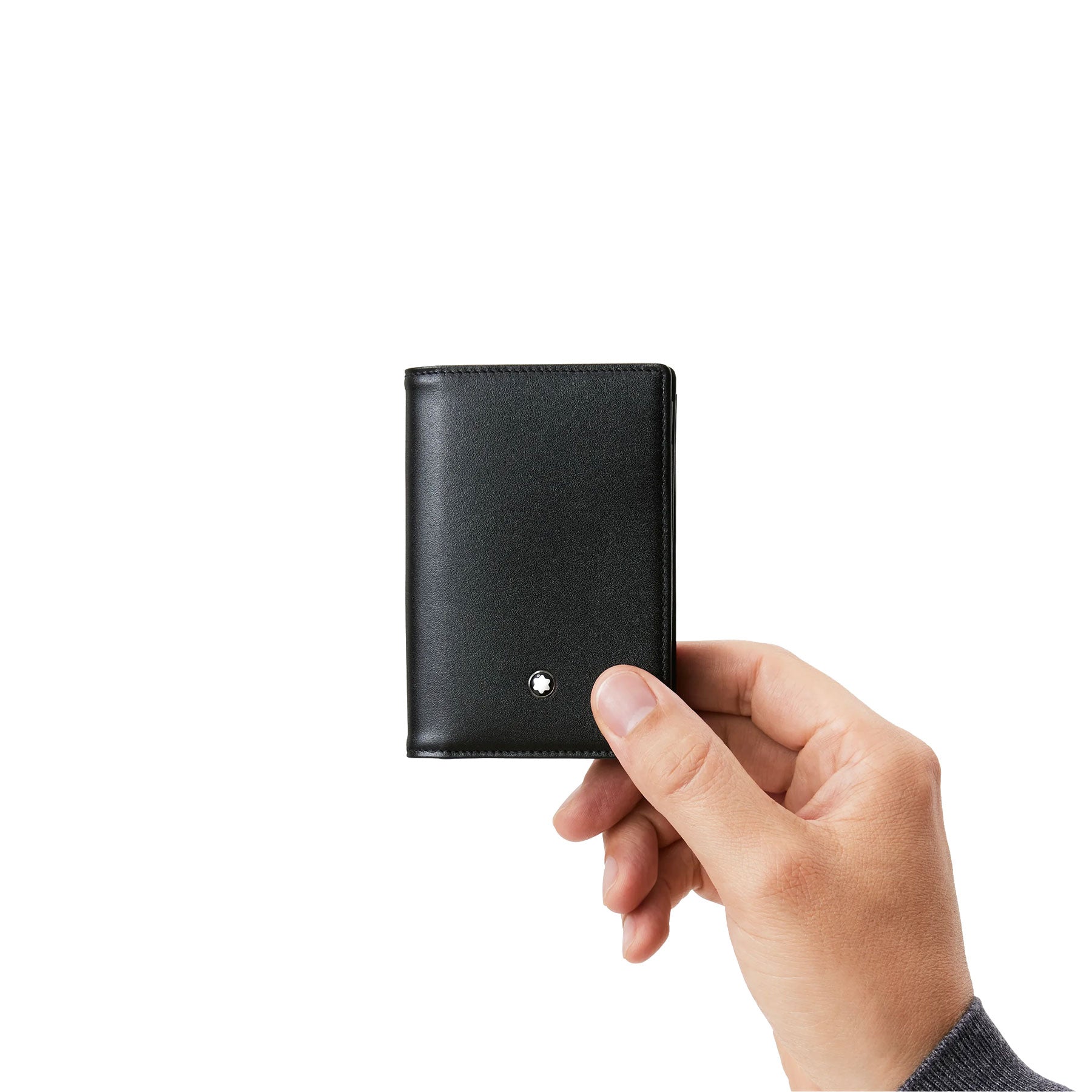 A hand holds the Montblanc Meisterstück Leather Business Card Holder against a plain white background. Crafted from sleek European full-grain cowhide, this black leather accessory features a minimalist design and is adorned with a small Montblanc emblem on the lower front corner, making it an elegant choice for storing business cards.
