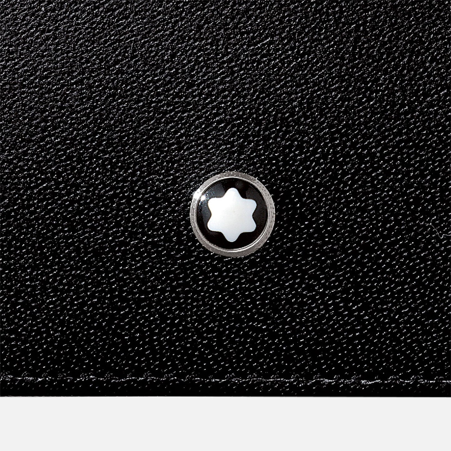 A close-up of the Montblanc Meisterstuck Leather Business Card Holder showcases its black textured surface, crafted from European full-grain cowhide, adorned with a small, round Montblanc emblem featuring a silver design and a white star-like symbol at its center.