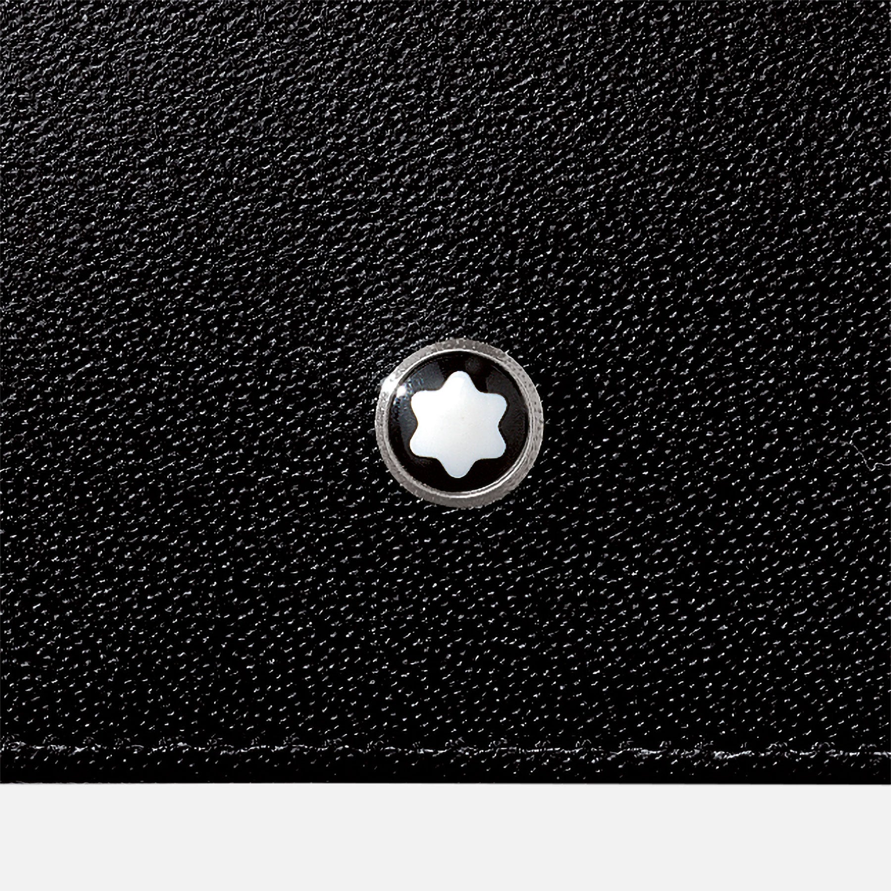 A close-up of the Montblanc Meisterstuck Leather Business Card Holder showcases its black textured surface, crafted from European full-grain cowhide, adorned with a small, round Montblanc emblem featuring a silver design and a white star-like symbol at its center.