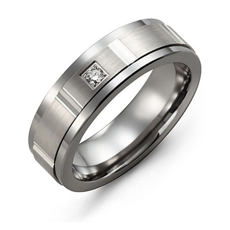 The Madani Tungsten and 10K White Gold Round Brilliant Diamond Wedding Band is a stylish men's ring, featuring a brushed matte finish with grooved detailing and subtle engraved lines. It is adorned with a small square diamond, offering a modern and elegant touch to its exquisite design.