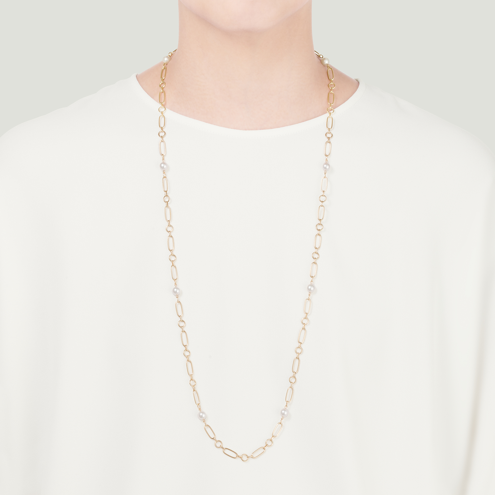 A person is wearing the Mikimoto M Code 18k Yellow Gold Akoya Cultured Pearl Necklace over a plain white top. The background is light gray.