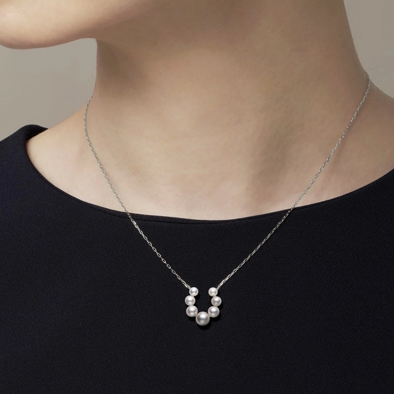 A person wearing the Mikimoto Bubbles 18K White Gold Pearl Necklace Pendant, which features a curved row of seven Akoya cultured pearls, paired with a simple black top.