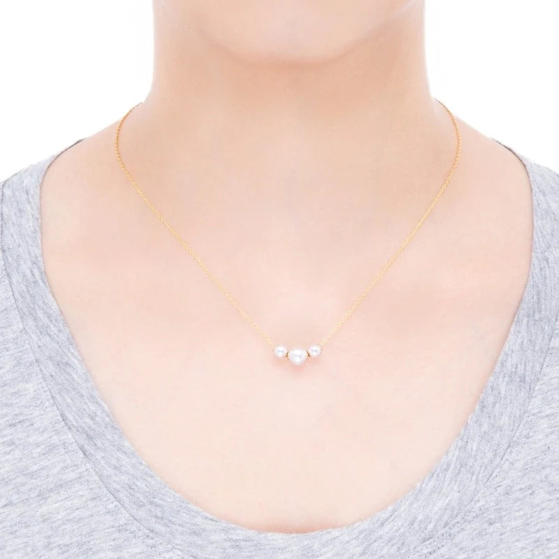 A person wearing a gray shirt and the Mikimoto Pearls In Motion 18K Yellow Gold Pearl Necklace Pendant, featuring three small white Akoya cultured pearls centered on their neck, against a plain white background.