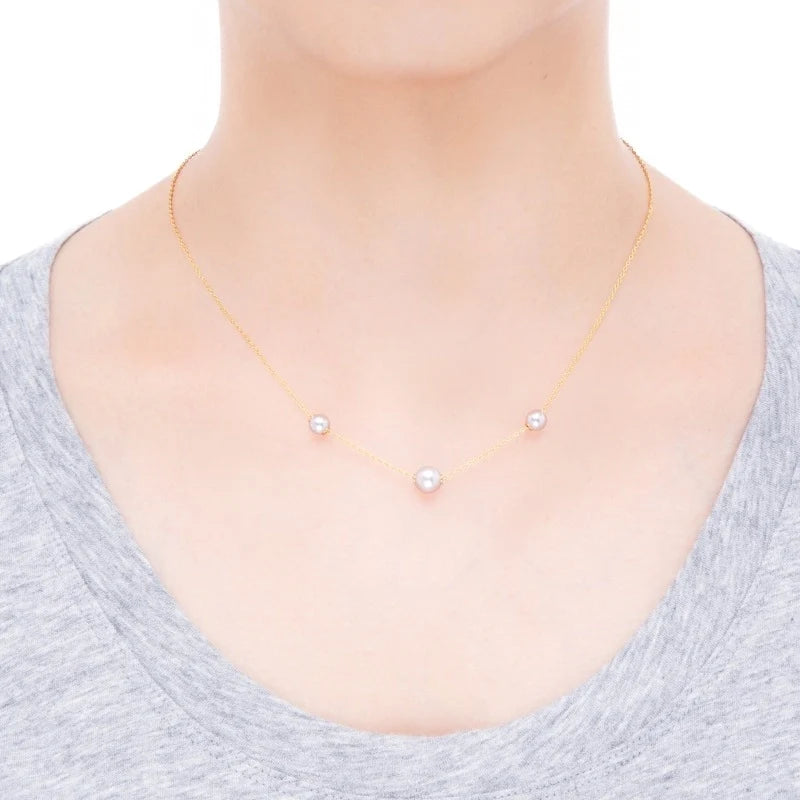 A person wearing a light gray shirt and the Mikimoto Pearls In Motion 18K Yellow Gold Pearl Necklace Pendant, which features three evenly spaced Akoya cultured pearls and showcases Mikimoto’s signature elegance.