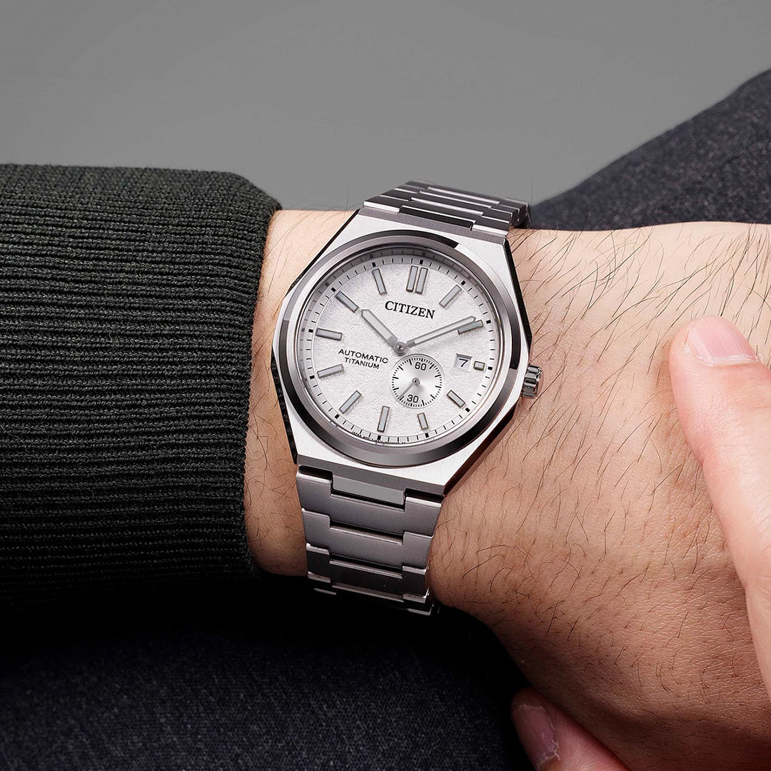 A person wears the CITIZEN Zenshin Mechanical Automatic 40.5mm Watch with a metal band and round face, featuring silver markers, hands, date window, and subdial, paired stylishly with a dark long-sleeve shirt.