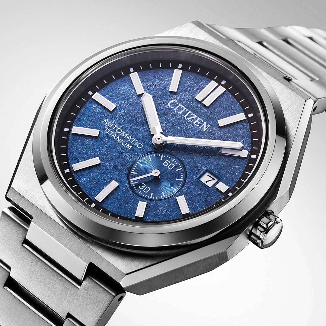 A close-up of the CITIZEN Zenshin Mechanical Automatic 40.5mm Watch, featuring a metallic band, blue textured dial, silver hour markers, a date window at 3 o’clock, and a subdial at 6 o’clock.