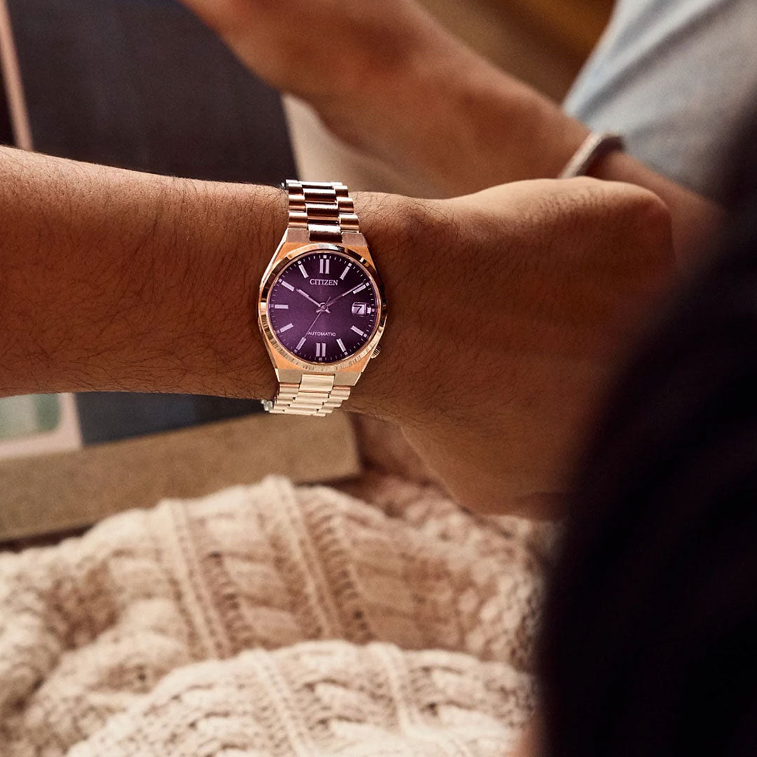 A person wearing a CITIZEN TSUYOSA Collection Automatic 37mm Watch with a silver band and purple face sits beside someone who has a knitted blanket on their lap.