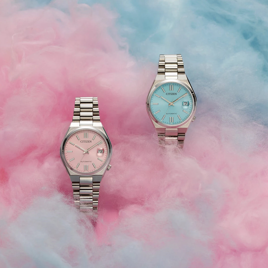 Two CITIZEN TSUYOSA Collection Automatic 37mm watches—one with a pastel pink dial, the other with a blue face—rest on fluffy pink and blue clouds. Both feature stylish stainless steel cases and showcase CITIZEN's signature design.