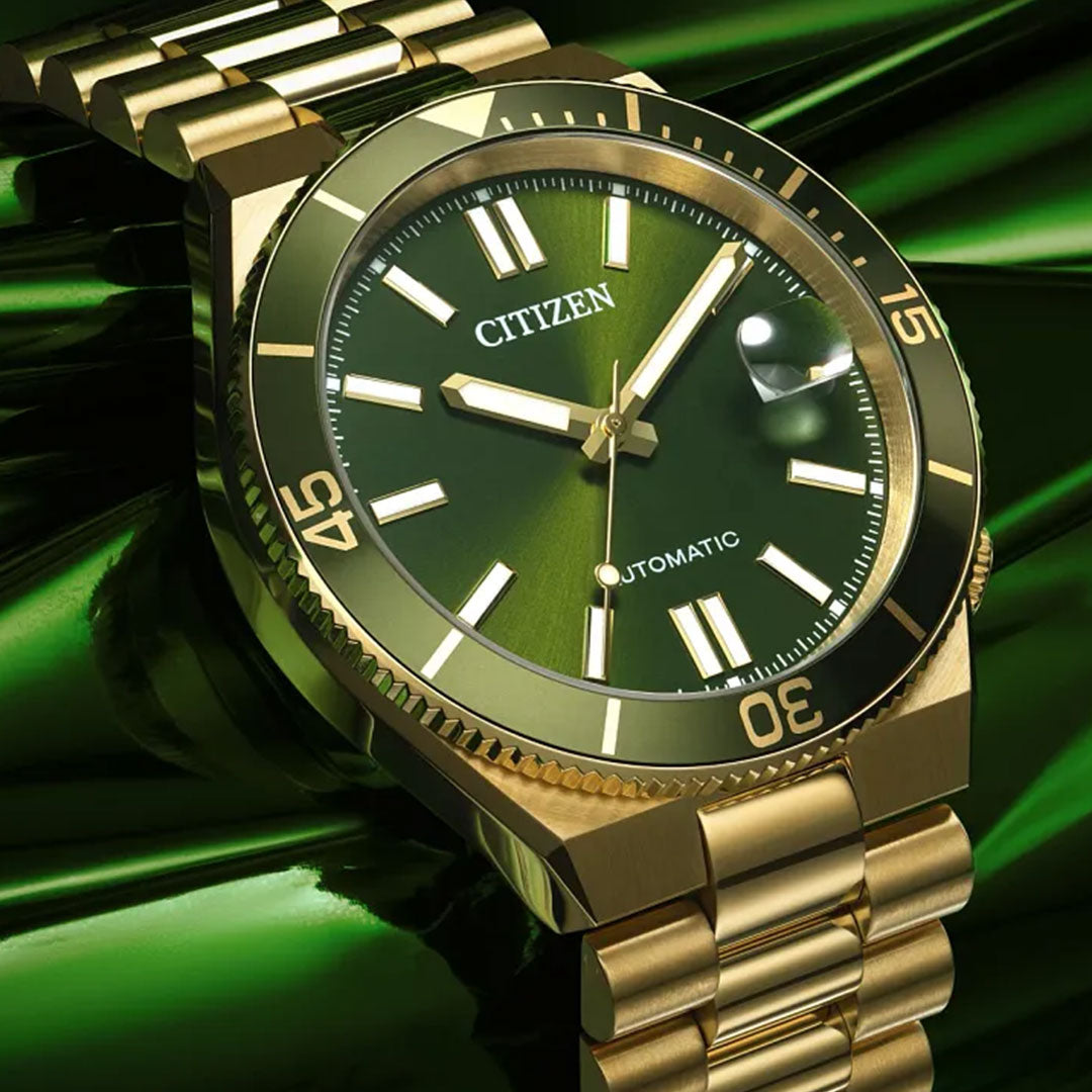 The CITIZEN TSUYOSA Shore Automatic 40mm Watch features a gold-tone stainless steel case, green dial with gold hour markers and white indices, and a polished metal band, all highlighted on a reflective green surface.