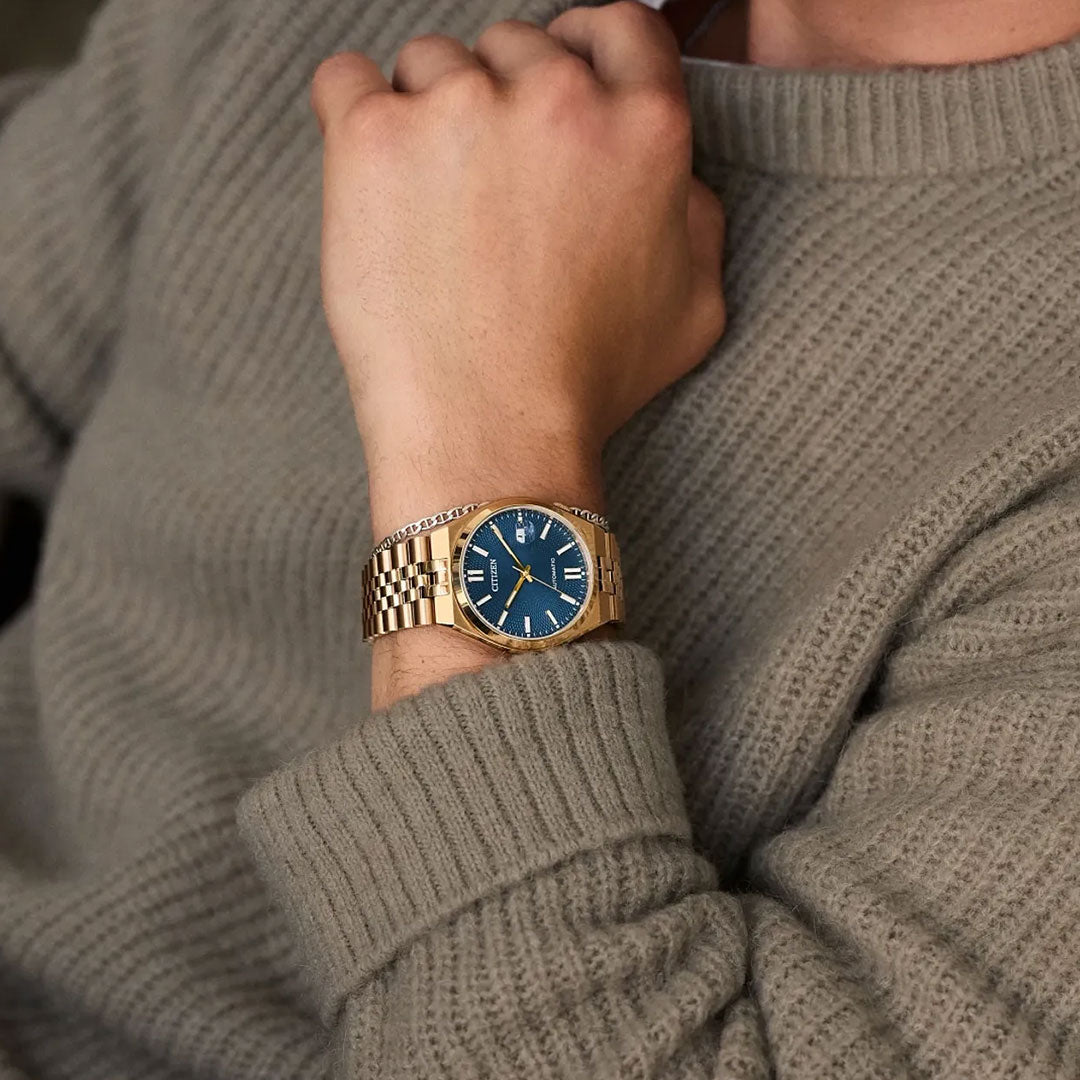 A person in a beige knitted sweater shows off a CITIZEN TSUYOSA 60 Automatic 40mm Watch—gold case, blue dial, metal band, Roman numeral markers, by CITIZEN.