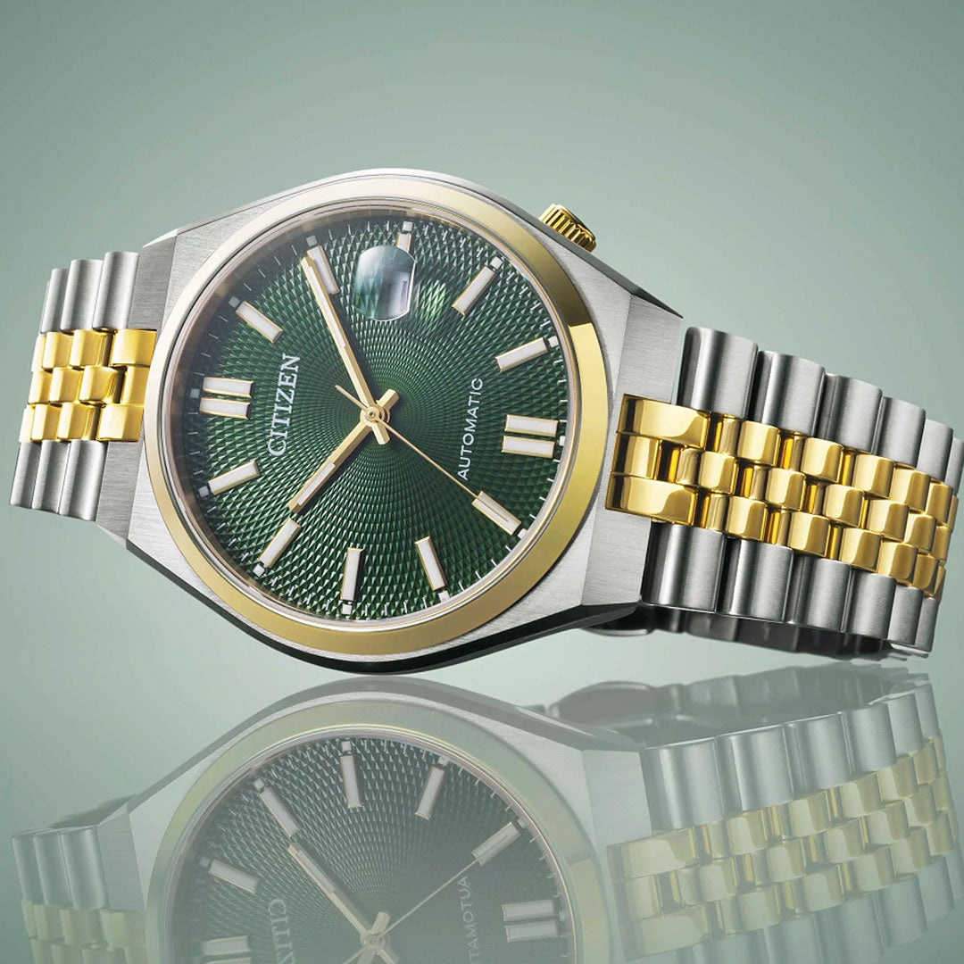 The CITIZEN TSUYOSA 60 Automatic 40mm Watch features a green dial, gold and silver stainless steel bracelet, gold bezel, and silver hour markers. It is showcased on a reflective surface with a soft green backdrop.
