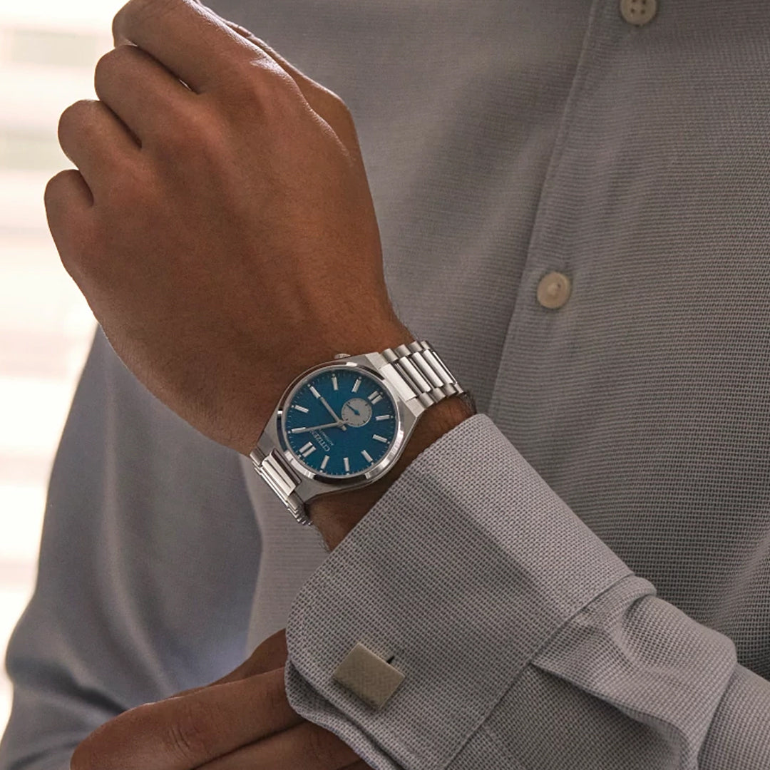 Wearing a CITIZEN TSUYOSA Small Second Automatic 40mm Watch with a silver band and blue face, a person adjusts the cuff of their light gray textured dress shirt.
