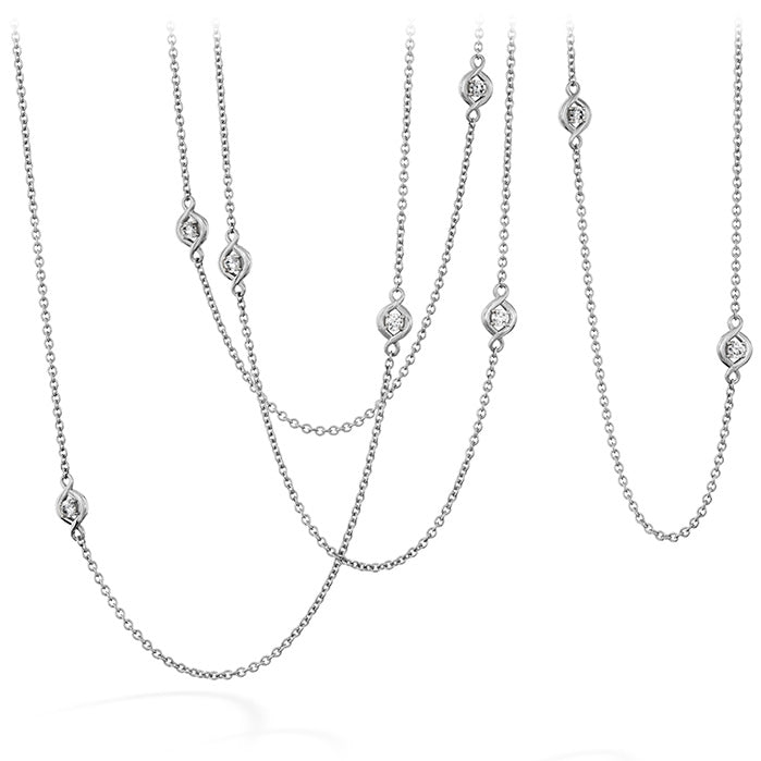 The Hearts on Fire Optima Station Necklace, with its elegant chain design and small oval pendants, is displayed against a white background. Made by Hearts on Fire, it offers options in 18 Karat White Gold, with some featuring dazzling diamonds for added sparkle. The varying lengths create a sophisticated layered look perfect for any occasion.