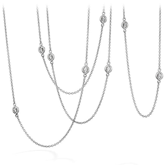 The Hearts on Fire Optima Station Necklace, with its elegant chain design and small oval pendants, is displayed against a white background. Made by Hearts on Fire, it offers options in 18 Karat White Gold, with some featuring dazzling diamonds for added sparkle. The varying lengths create a sophisticated layered look perfect for any occasion.