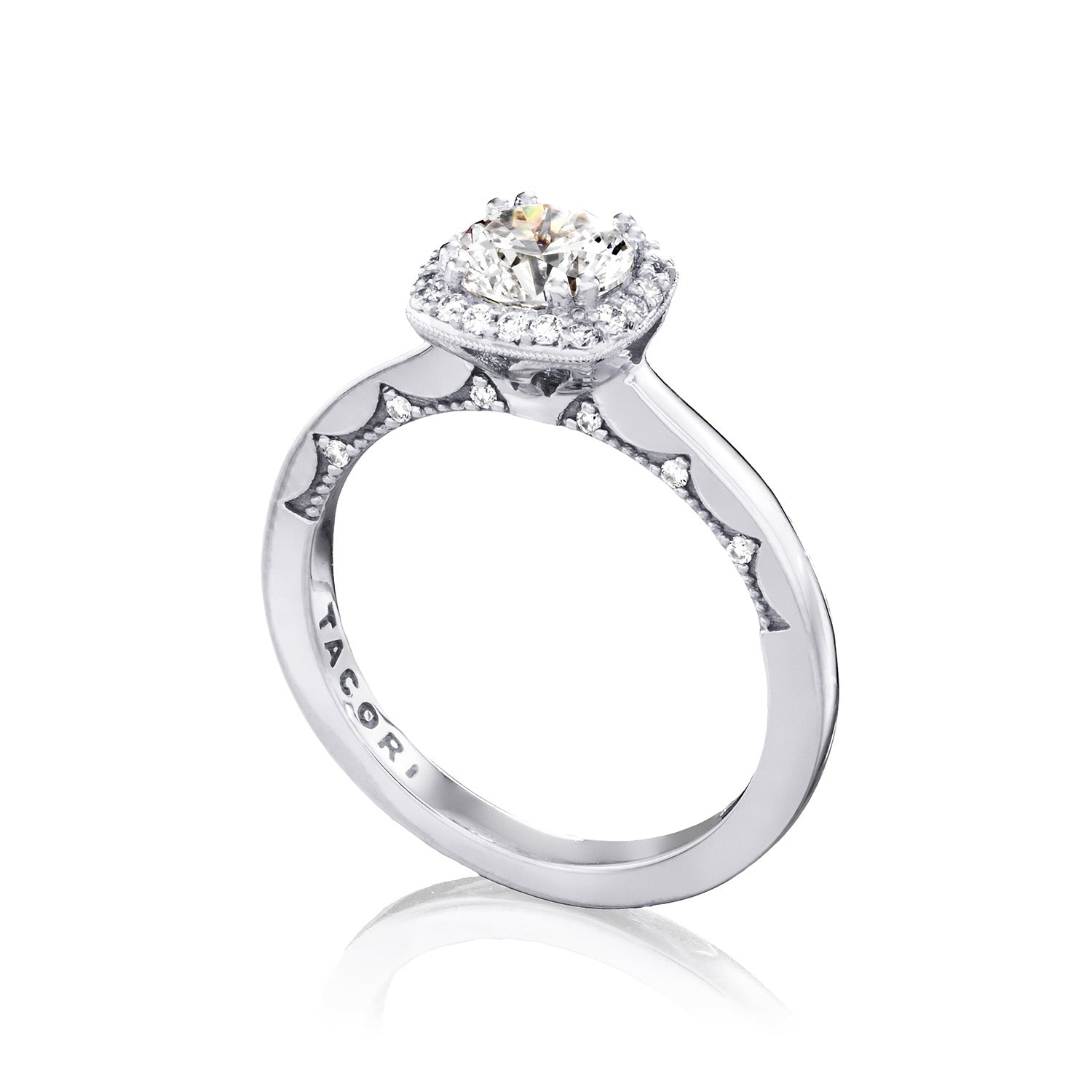The Tacori Coastal Crescent engagement ring in 14K white gold features a central large round brilliant diamond, surrounded by a halo of smaller diamonds. The band is intricately detailed and engraved with "TACORI," embodying elegance and timeless beauty.