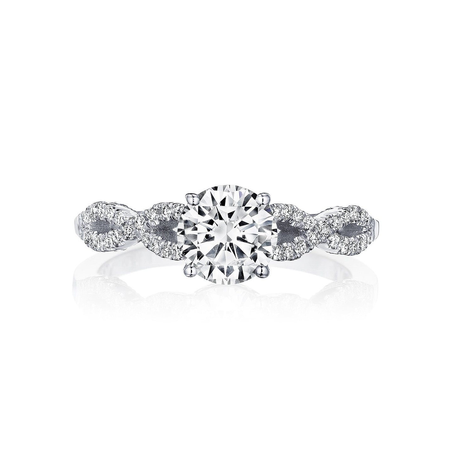 The Tacori Coastal Crescent 14K White Gold Round Brilliant Solitaire Semi Mount with Diamond Band Engagement Ring exudes elegance. Expertly crafted by Tacori gemologists, it features a large round diamond at the center and an intricately designed band adorned with smaller diamonds that form detailed patterns reminiscent of a Coastal Crescent, all set against a plain white background.