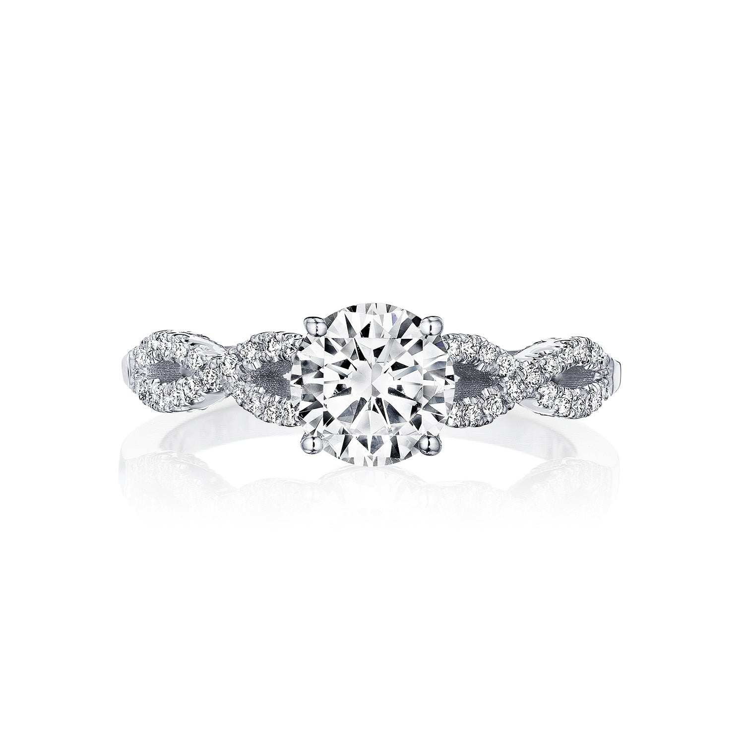 The Tacori Coastal Crescent 14K White Gold Round Brilliant Solitaire Semi Mount with Diamond Band Engagement Ring exudes elegance. Expertly crafted by Tacori gemologists, it features a large round diamond at the center and an intricately designed band adorned with smaller diamonds that form detailed patterns reminiscent of a Coastal Crescent, all set against a plain white background.