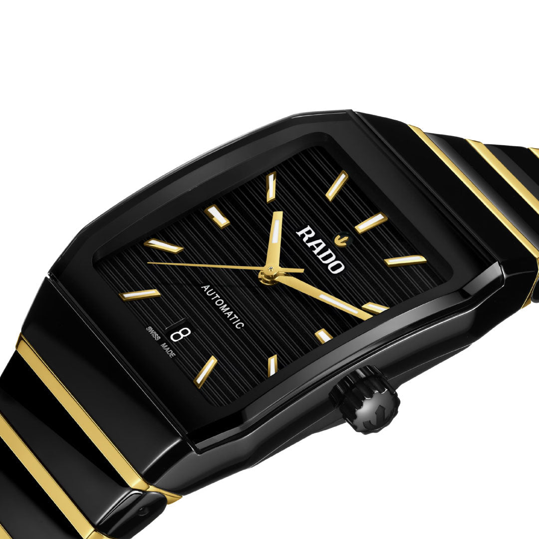 A close-up of the RADO Anatom Automatic 32.5mm watch featuring a sleek black and gold rectangular face, gold hour markers and hands, sapphire crystal, date at 6 o'clock, and a black and gold high-tech ceramic bracelet.