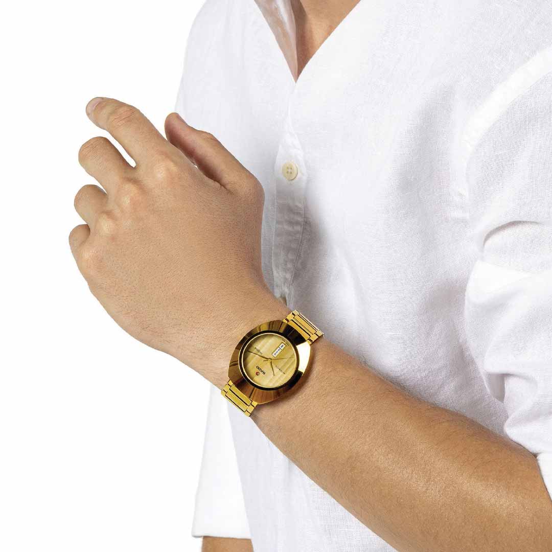 A person in a white shirt is displaying their right wrist, adorned with a RADO DiaStar Original Automatic 38mm Watch. This exquisite timepiece boasts an automatic movement and gleams with a stylish yellow gold design, complete with a date display.