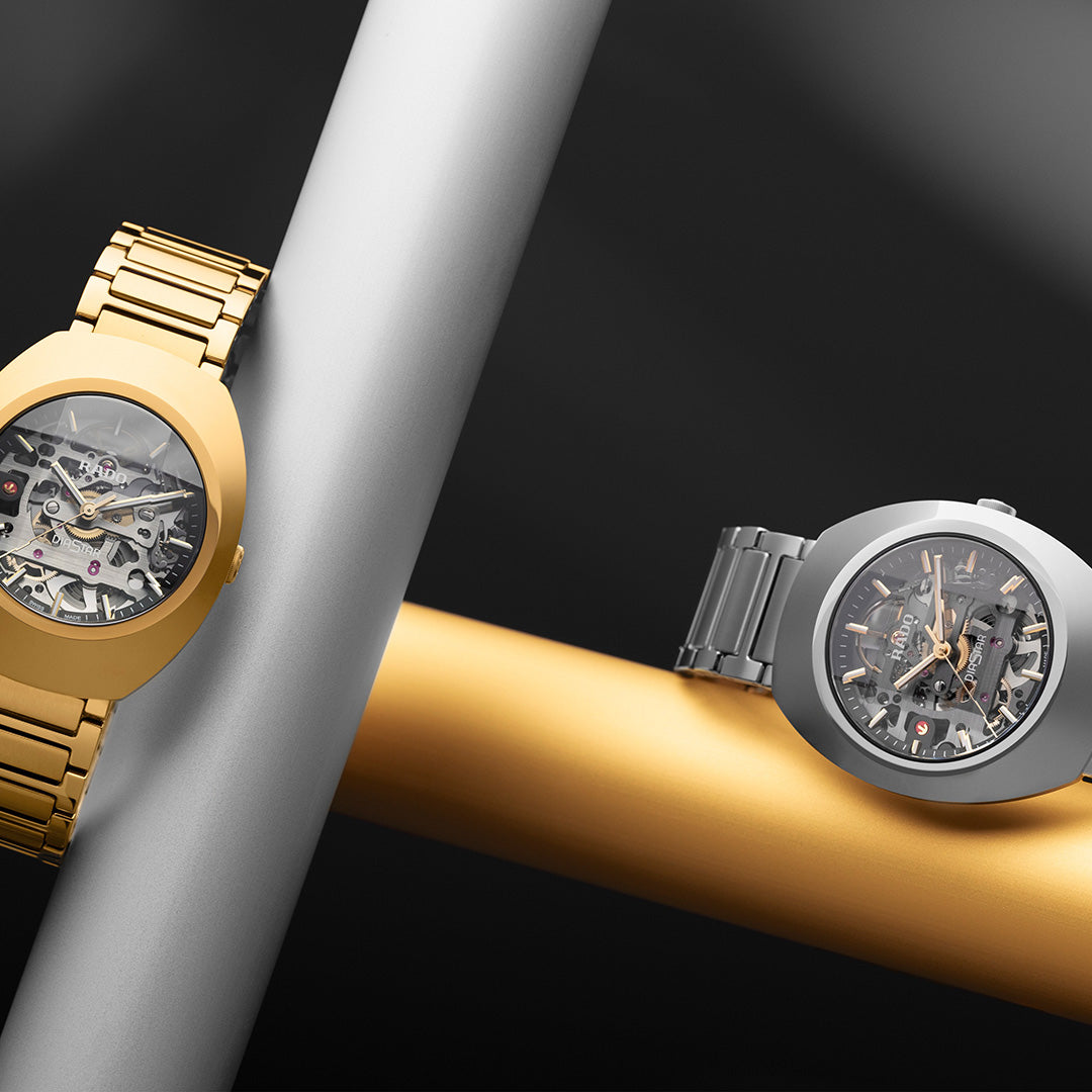 Two luxury skeleton watches, including the RADO DiaStar Original Skeleton Automatic 38mm Watch with automatic calibre and a gold-coloured Ceramos bezel, are displayed diagonally on metallic rods against a dramatic black background.