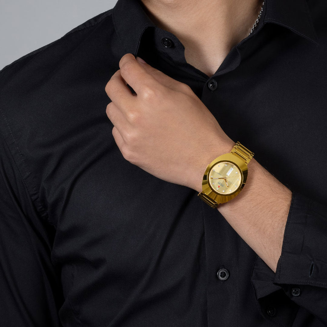 Wearing a black button-up shirt, a person adjusts their collar, showcasing the RADO DiaStar Original Automatic 38mm Watch in yellow gold on their wrist.