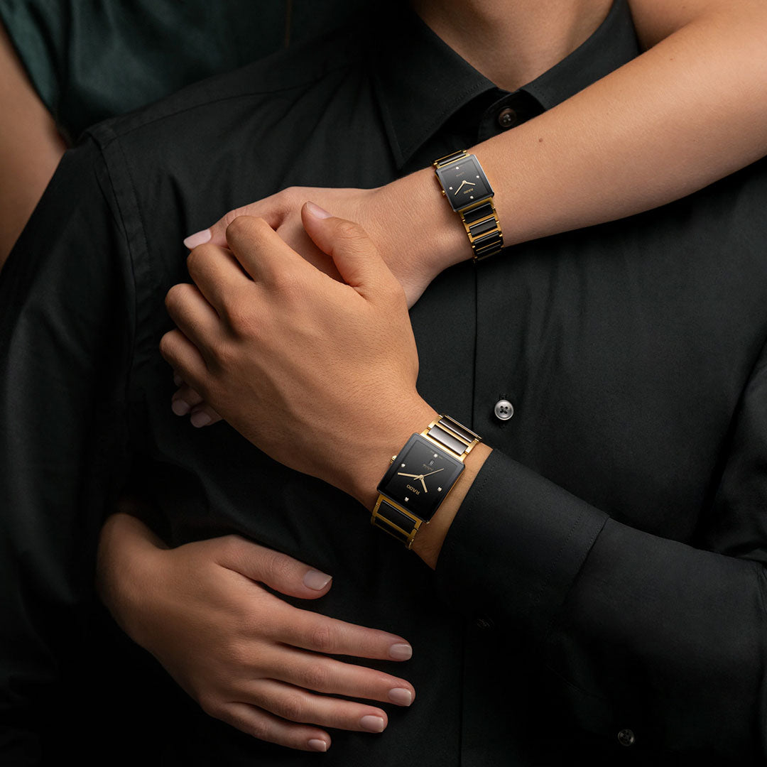 Two people in black embrace, both wearing the RADO Integral Diamonds Quartz 23mm Watch. Their arms wrapped around each other highlight the high-tech ceramic finish and their close connection.
