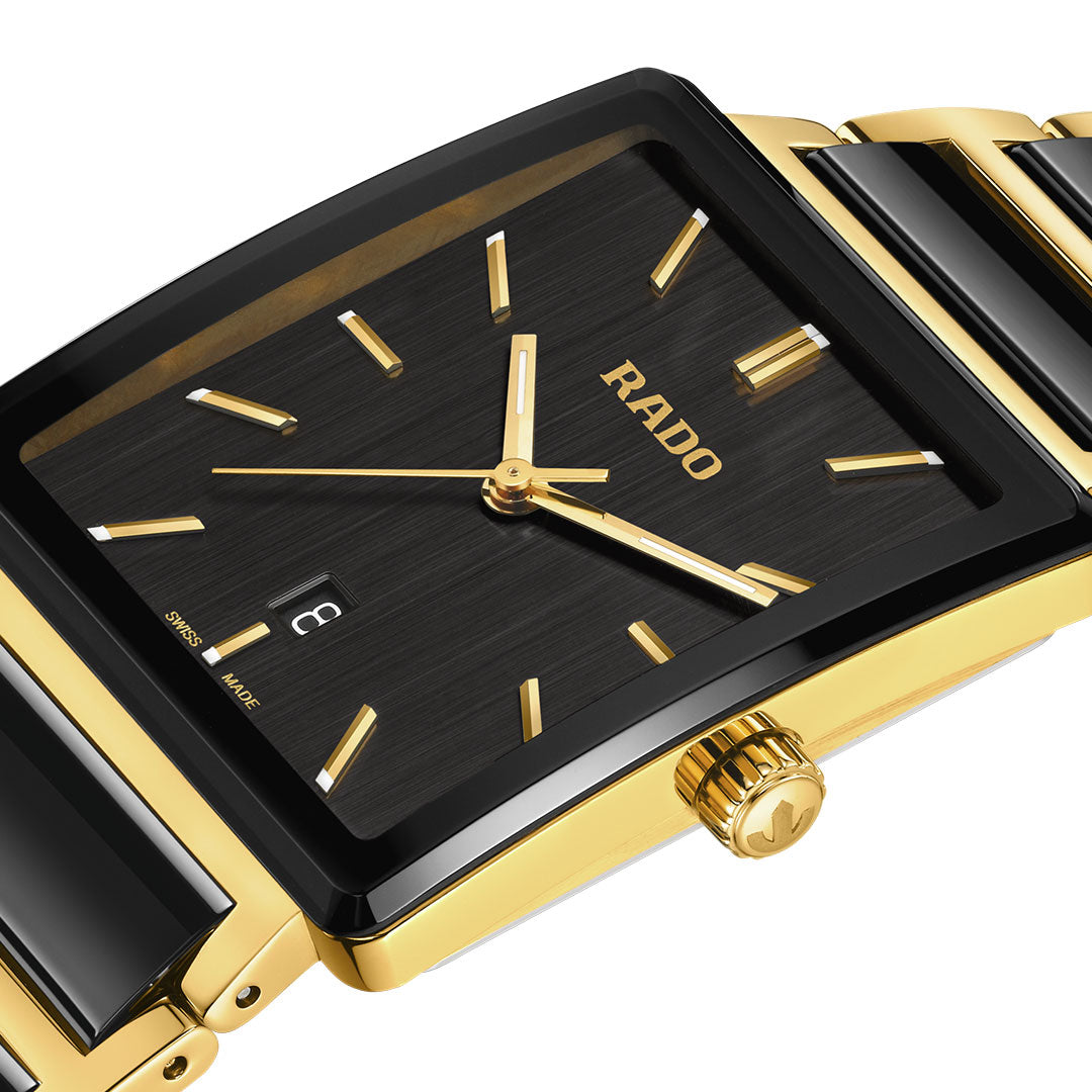 A close-up of the RADO Integral Quartz 31.5mm Watch featuring a rectangular black dial with gold markers and hands, a date window, and a gold and black stainless steel bracelet. The case and crown are elegantly finished in gold-tone.