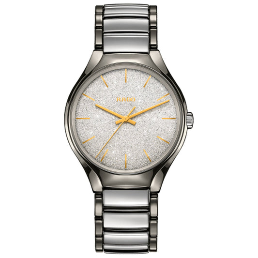 The RADO True Blaze Automatic 40mm Watch boasts a sleek design, featuring a silver band and a sparkling silver dial protected by scratch-resistant sapphire crystal. Its face is elegantly adorned with minimalistic gold hour markers and hands, alongside the brand logo at the 12 o'clock position, encapsulating an elegant and refined design.