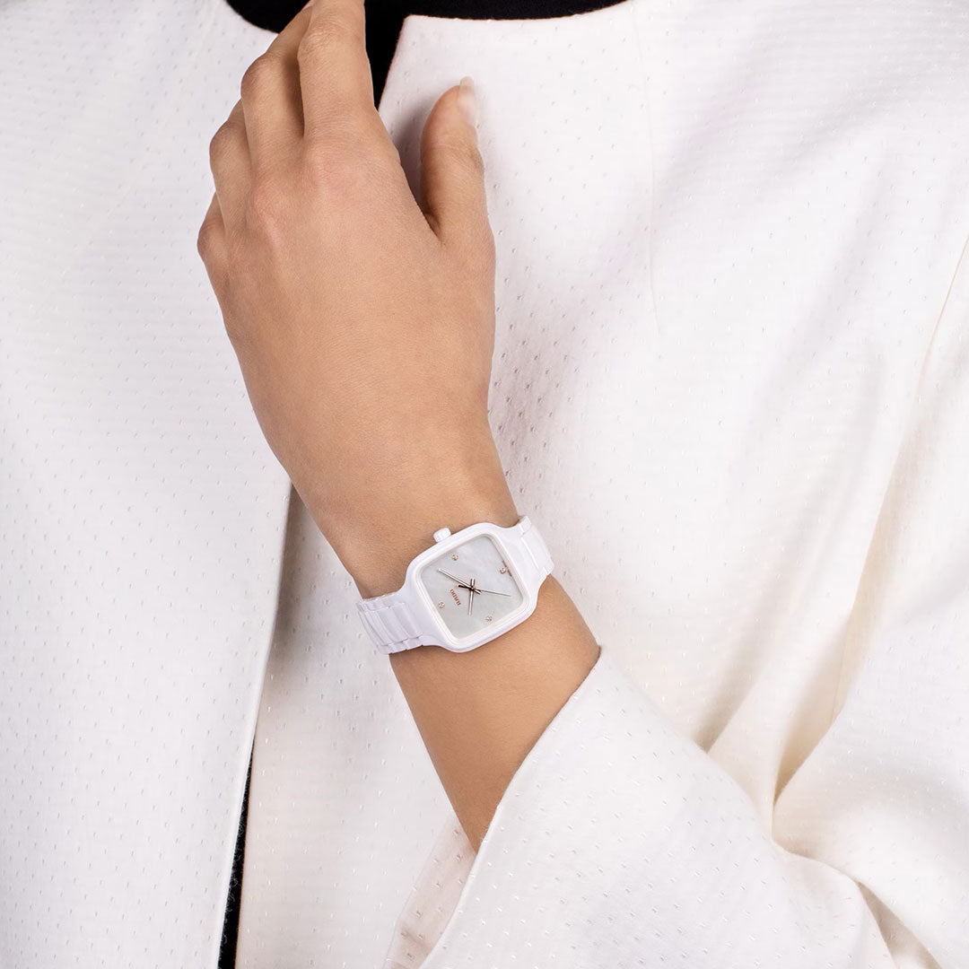 A person in a white textured jacket showcases a RADO True Square Diamonds Quartz 29mm Watch on their left wrist, with their hand resting near their collarbone.