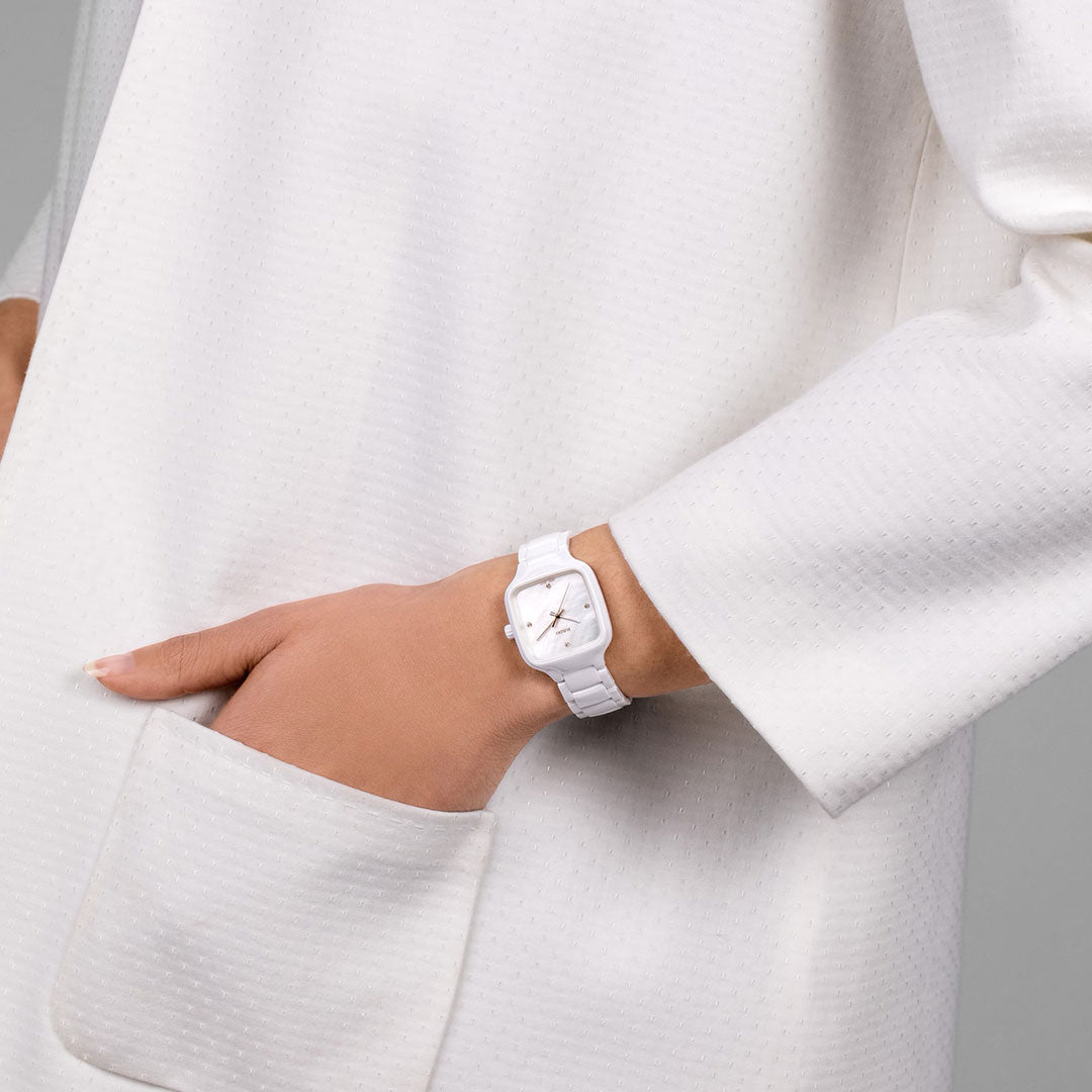 A person in a textured white coat with one hand in the pocket showcases the RADO True Square Diamonds Quartz 29mm Watch, a minimalist square timepiece crafted by RADO with high-tech ceramic and elegant diamond accents.