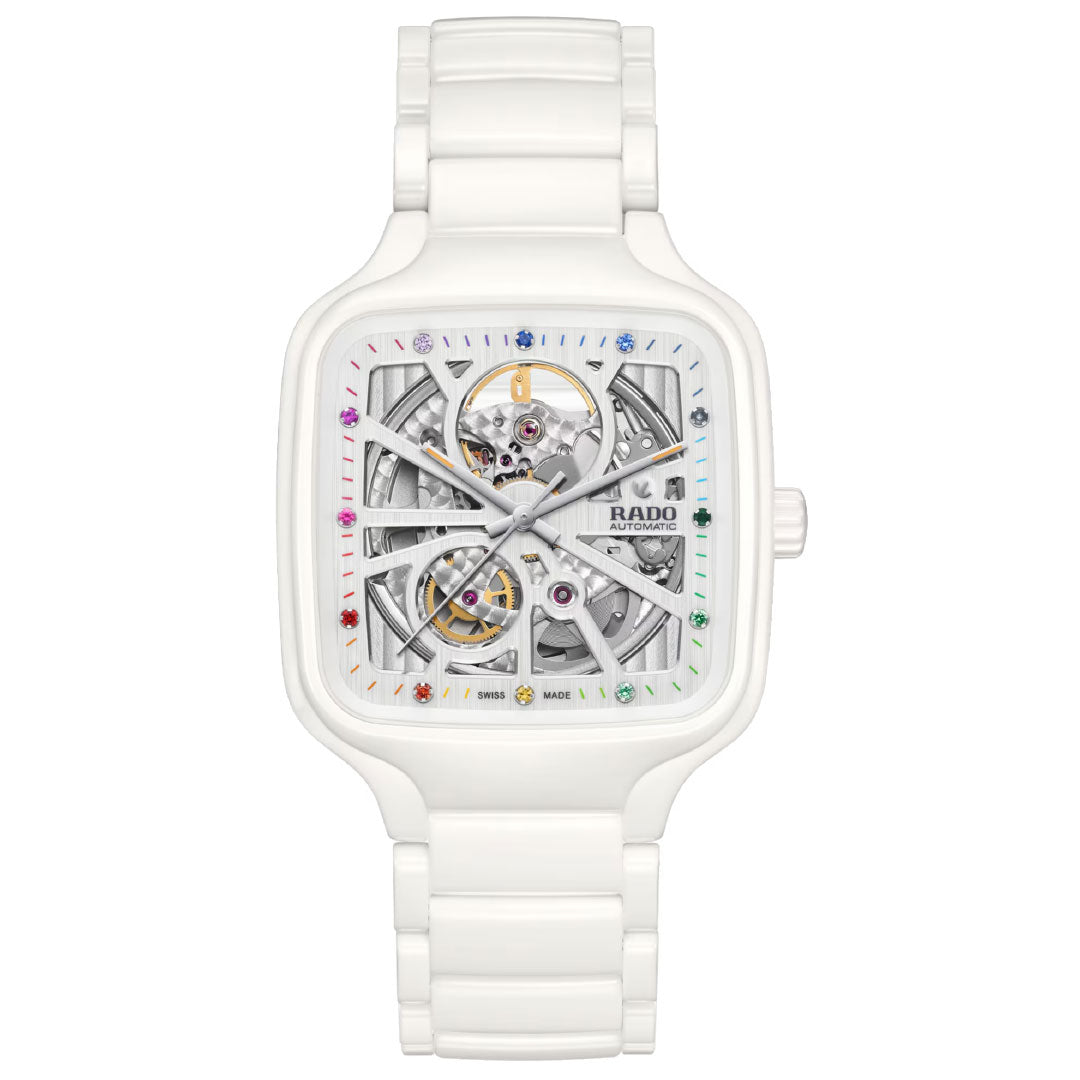 The RADO True Square Automatic Open Heart 38mm watch features a white high-tech ceramic case, square skeleton dial with visible inner workings and colorful gemstone markers, and a glossy bracelet that highlights its distinctive open-heart design.