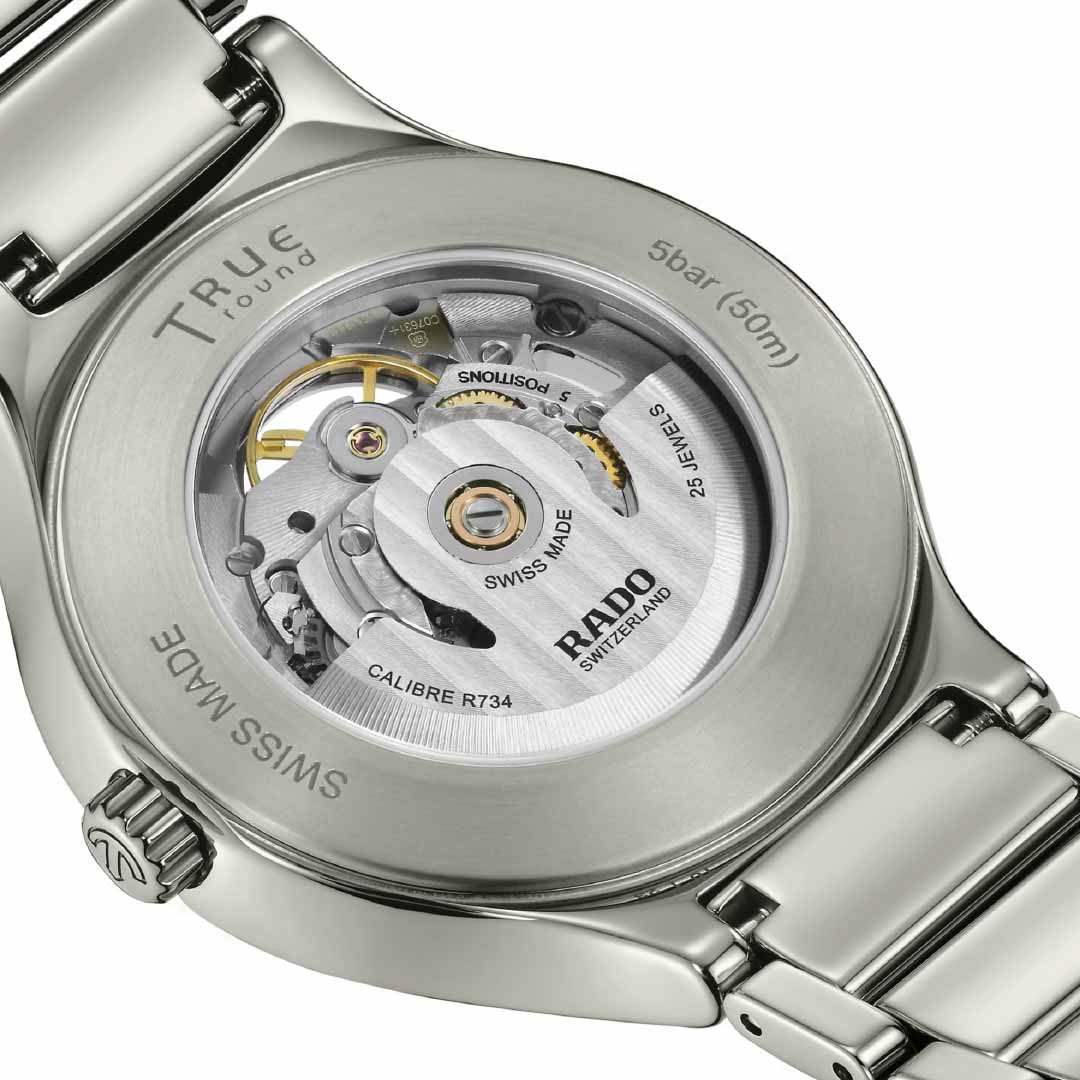 The close-up of the RADO True Round Automatic Open Heart 40mm watch back showcases its transparent case, revealing the intricate craftsmanship of the automatic movement inside. Engraved with "True Round" and "5 bar (50m)" on its stainless steel back, it elegantly complements a high-tech ceramic bracelet.