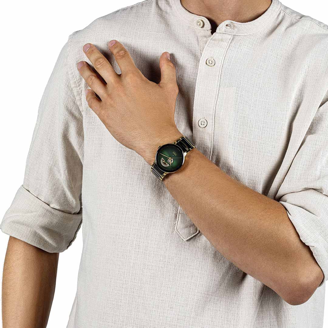 A person in a beige button-up shirt with rolled-up sleeves displays a RADO Centrix Automatic Open Heart 39.5mm Watch on their left wrist, featuring a green face and metallic band, offering an impressive 80-hour power reserve. Their right hand gently rests on their chest.