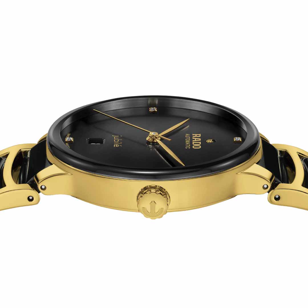 A detailed view of the RADO Centrix Diamonds Automatic 39.5mm Watch showcases its elegant gold and black design, featuring yellow gold-colored stainless steel seen from the side profile. The timepiece is distinguished by a black dial adorned with gold hour markers, an antimagnetic Nivachron™ hairspring, a date window, and a gold crown embossed with the brand's logo. Both the strap and case gleam in an exquisite gold tone.