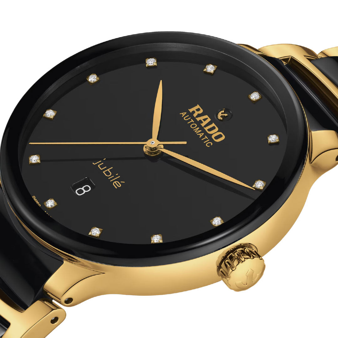A close-up of the RADO Centrix Automatic Diamonds 39.5mm watch featuring a black dial with diamond hour markers, yellow gold-coloured stainless steel accents, a date window at 6 o’clock, and a bracelet with black high-tech ceramic links.