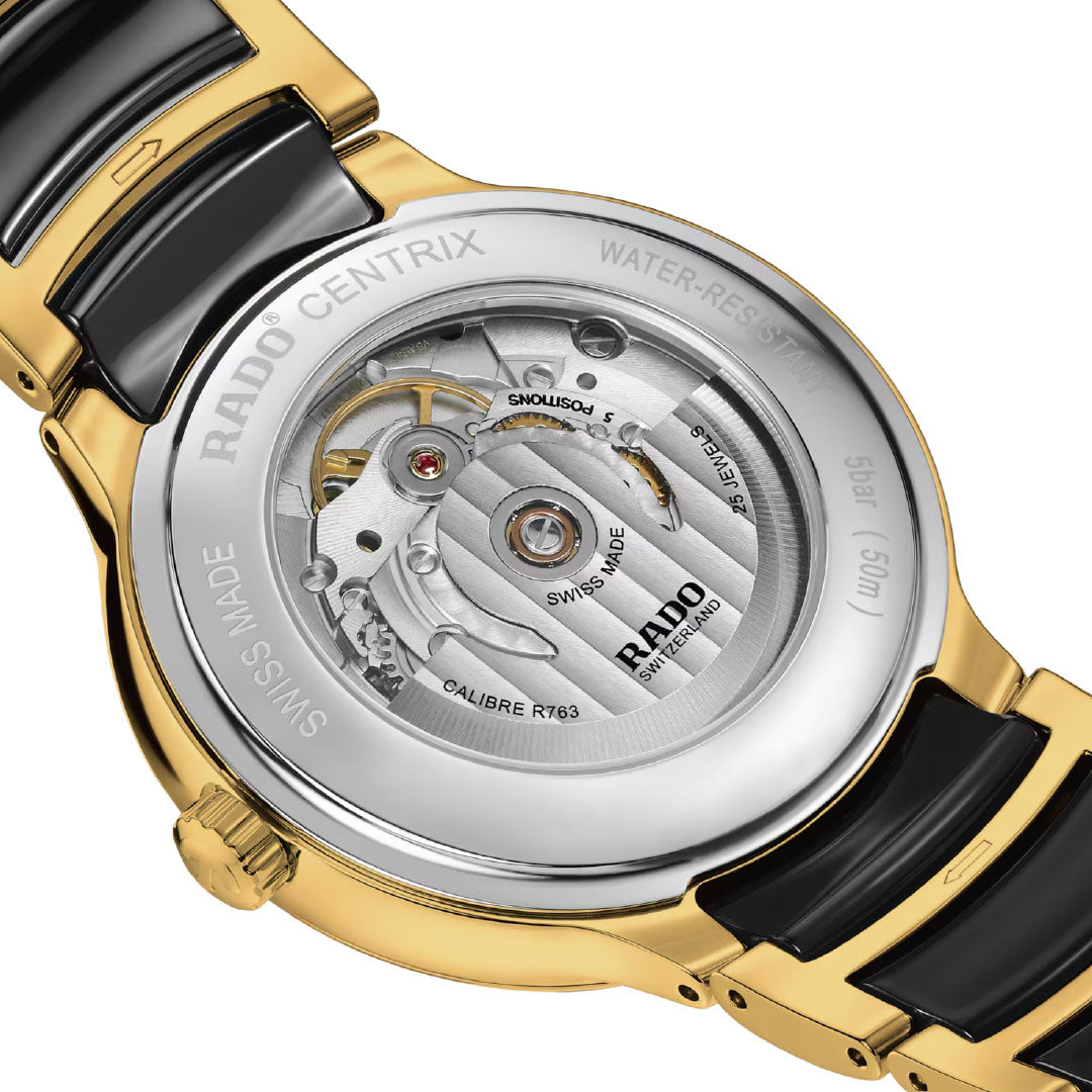 Close-up of the RADO Centrix Automatic Diamonds Automatic 39.5mm Watch’s transparent case back reveals its movement, with a bracelet combining yellow gold-coloured stainless steel and black high-tech ceramic, plus engraved text on the edge.