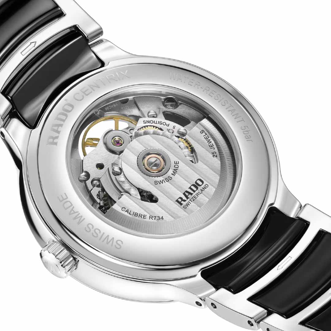 A detailed view of the RADO Centrix Open Heart Automatic 39.5mm Watch reveals its exposed mechanical movement, featuring engravings such as "25 JEWELS" and "SWISS MADE." The silver casing accentuates the intricate gears, Nivachron hairspring, and internal components, with an impressive 80-hour power reserve.