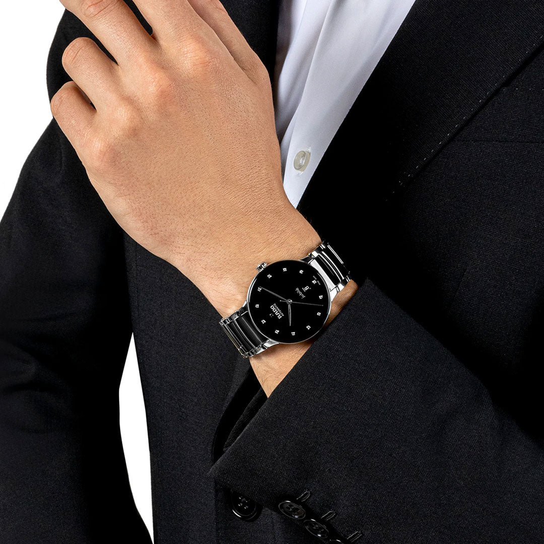 A person wearing a black suit and a RADO Centrix Automatic Diamonds 39.5mm watch, featuring automatic movement.
