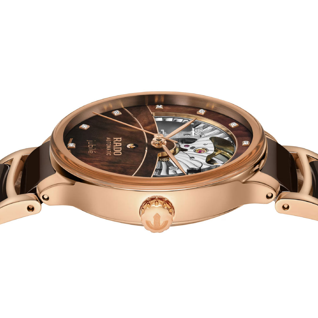 A close-up side view of the RADO Centrix Automatic Diamonds Open Heart 35mm Watch reveals its rose gold ceramic design, diamond hour markers, and a partially open dial with brown and gold-accented bezel and strap.