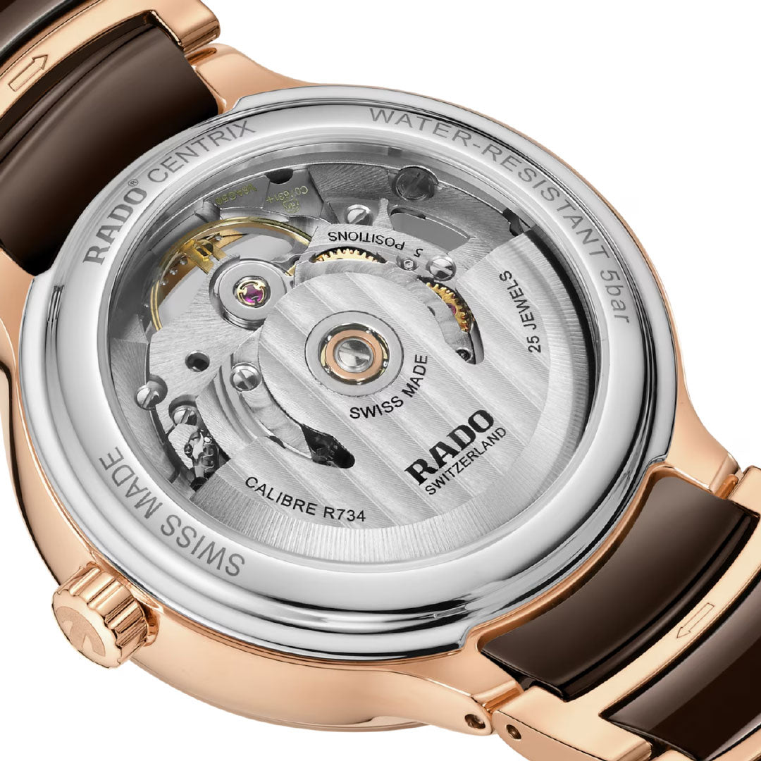 Close-up of the RADO Centrix Automatic Diamonds Open Heart 35mm Watch’s transparent caseback, showcasing its exposed automatic movement, rose gold ceramic case, brown strap, and engraved RADO branding and specifications.