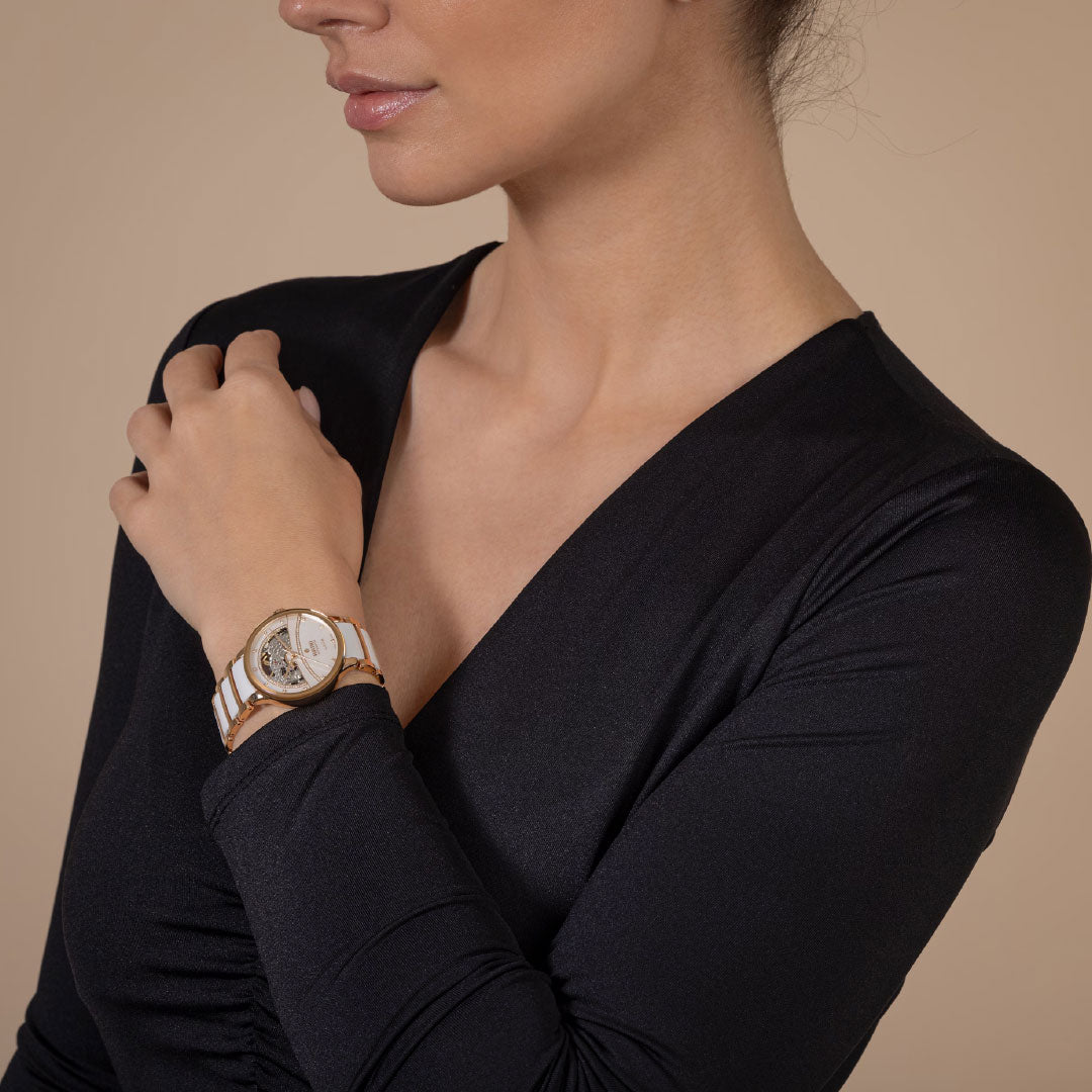 A woman in a black V-neck top poses with her left hand on her right shoulder, elegantly showcasing the RADO Centrix Automatic Diamonds Open Heart 35mm Watch against a neutral background.