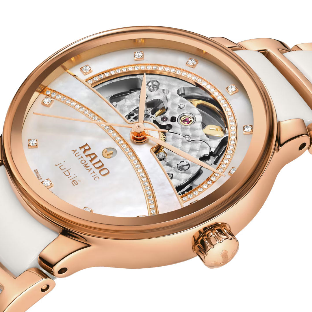 Close-up of the RADO Centrix Automatic Diamonds Open Heart 35mm watch, featuring a rose gold case, white strap, visible inner mechanics, diamond hour markers, gold accents on the dial, and "jubile" text.