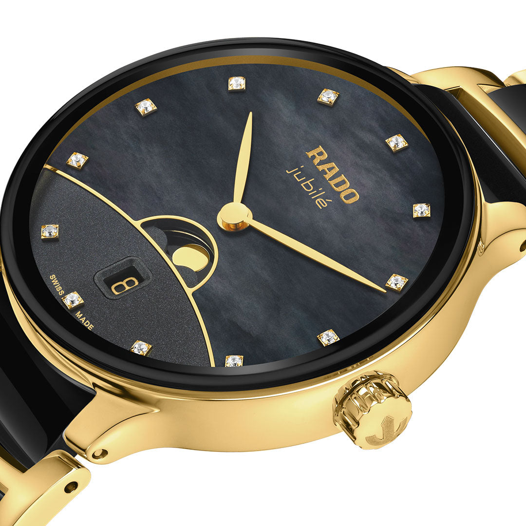 A close-up of the RADO Centrix Moonphase Quartz 35mm Watch featuring a gold and black design, diamond hour markers, black dial with moonphase complication, date window, gold crown, and elegant details.