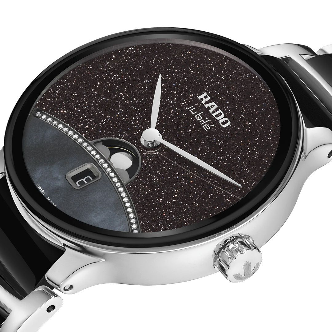 Close-up of the RADO Centrix Moonphase Quartz 35mm Watch featuring a sparkling black dial, silver-tone hands, date display, and crystal accents. Its metallic case and partially visible high-tech ceramic band enhance its elegance.