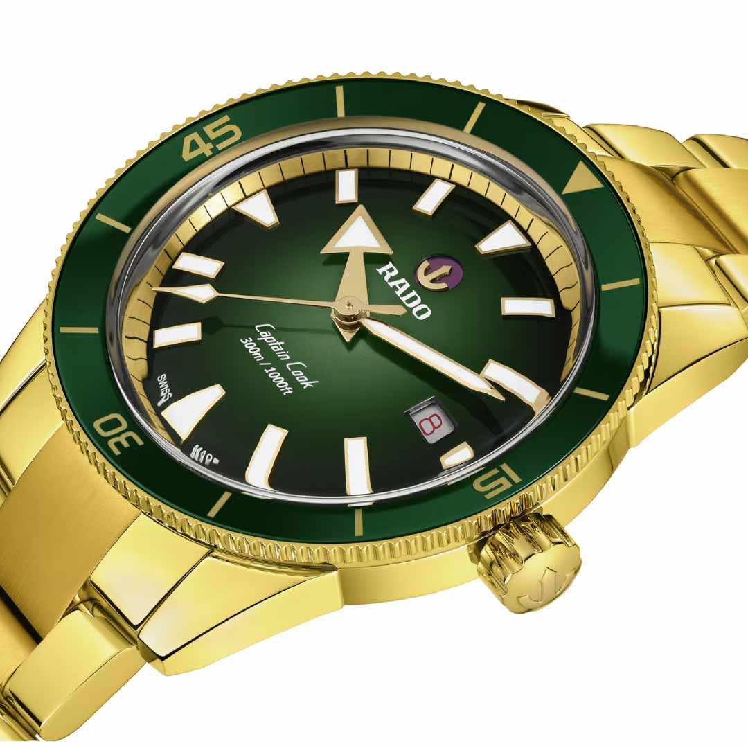 Introducing the RADO Captain Cook Automatic 42mm Watch, a stunning timepiece featuring a gold design with a striking green bezel and dial. It is adorned with white and gold hour markers and showcases the iconic "Rado" branding on the dial. Powered by automatic movement, it includes a date display for added functionality. The elegant gold bracelet enhances its stylish look while complementing its water-resistant design.