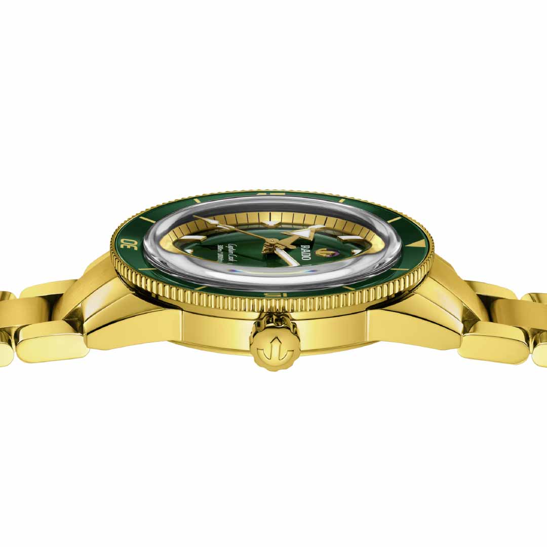 The RADO Captain Cook Automatic 42mm Watch, with its green dial viewed from the side, highlights an elegant design. It features a yellow gold-colored bezel, a gold strap, and an intricate crown. Ensuring precision and timeless sophistication is the Rado R763 automatic movement.